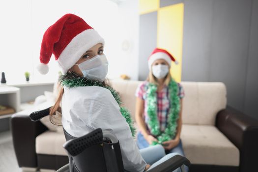 Portrait of young woman visit friend in hospital, relative in wheelchair, face mask for protection. Health, medicine, disability, nursing house concept
