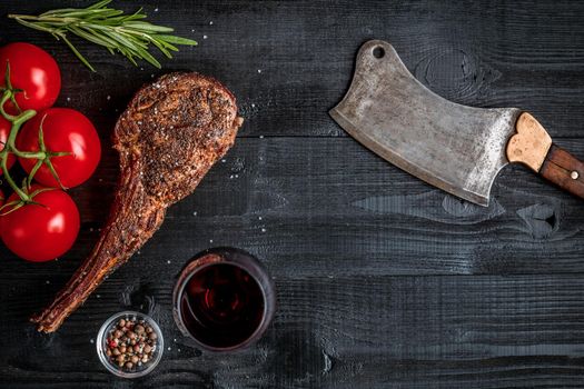 Barbecue dry aged rib of beef with spice, vegetables and glass of red wine close-up on black wooden background. Top view. Copy space. Still life. Flat lay