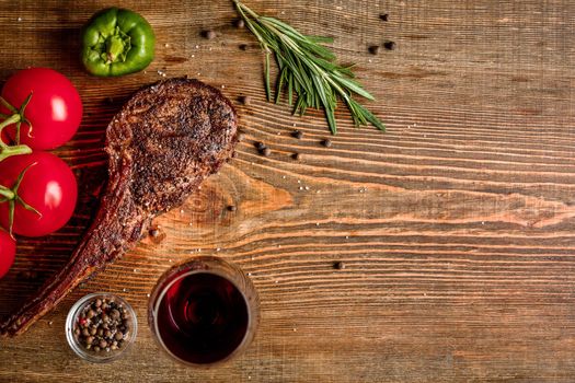 Barbecue dry aged rib of beef with vegetables and glass of red wine close-up on wooden background. Top view. Copy space. Still life. Flat lay