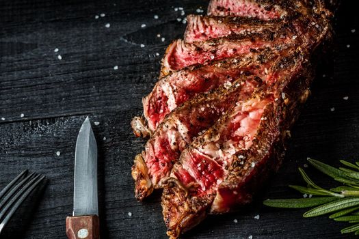 Barbecue dry aged rib of beef with spice, close-up on black wooden background. Top view. Copy space. Still life. Flat lay