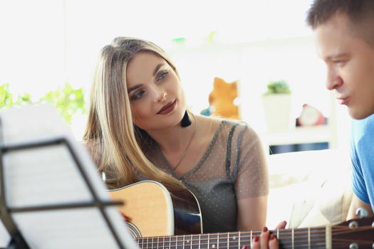 Portrait of woman teaching man how to play on guitar instrument, music class at home. Female explain chords and melody. Music, art, hobby, leisure concept