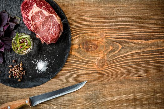 Dry aged raw beef steak with ingredients for grilling on wooden background. Top view. Copy space. Still life. Flat lay