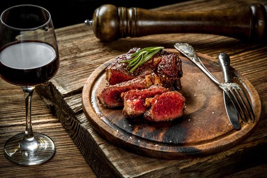 Grilled ribeye beef steak with red wine, herbs and spices on wooden table. Still life