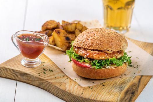 Fast food dish. Appetizing meat burger, potato chips and sauce. Takeaway composition. French fries, hamburger and sauce on wooden board.