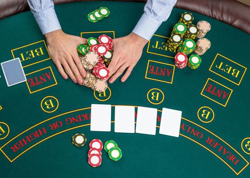 Close up of poker player with playing cards and chips at green casino table, view from above.