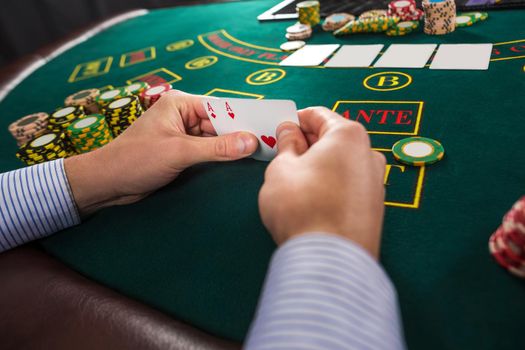 Male poker player holding the of two cards aces at green casino table