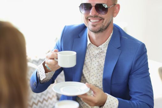 Portrait of well dressed smiling man drinking coffee in cafe on business meeting with partner. Cheerful middle aged guy in posh suit. Lunch, deal concept