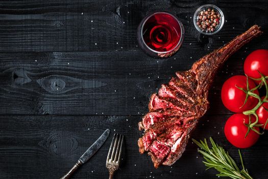 Barbecue dry aged rib of beef with spice, vegetables and glass of red wine close-up on black wooden background. Top view. Copy space. Still life. Flat lay