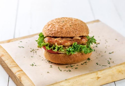 Close-up of home made burger on wooden board. A white wooden table