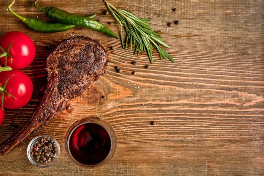 Barbecue dry aged rib of beef with vegetables and glass of red wine close-up on wooden background. Top view. Copy space. Still life. Flat lay