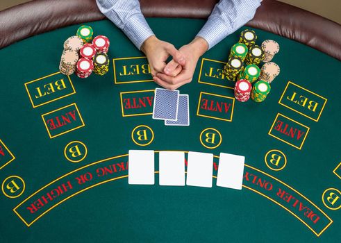 Close up of poker player with playing cards and chips at green casino table, view from above.