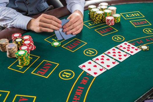 Close up of poker player with playing cards and chips at green casino table