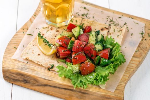 Vegetable salad with greens on a wooden board. A glass of light beer and salad on a white wooden table