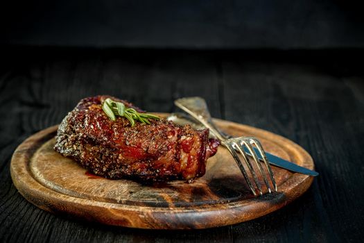 Barbecue Dry aged Ribeye Steak with knife and fork on cutting board. Black wooden background. Still life. Copy space. Close-up