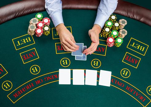 Close up of poker player with playing cards and chips at green casino table, view from above.