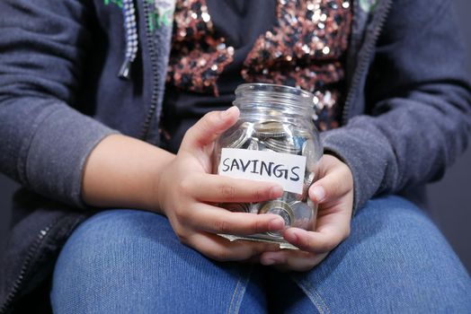 5 year old kid hand hold a saving coins jar .