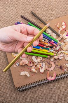 Hand holding Color Pencil over a notebook with pencil shavings