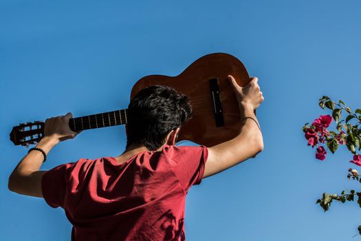 Young man rising an accoustic guitar in the blue sky