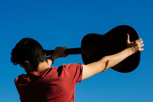 Young man rising an accoustic guitar in the blue sky