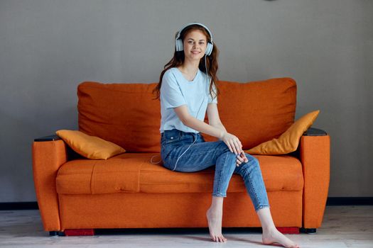 smiling woman sitting on the couch at home listening to music on headphones apartments. High quality photo