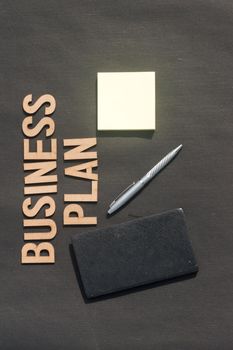 Businessman hand placing a pen and notebook in front of Word Business Plan made of wooden blocks of Alphabet letters. High Angle View. Vertical background. Close up