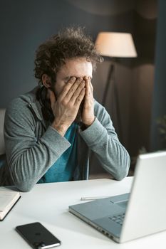 Tired Man Hiding his Eyes with Hands. He has Pain in his Eyes Because of Long-term Work at the Computer. Work Desk, Open Laptop, Mobile Phone. Close-up. High quality photo