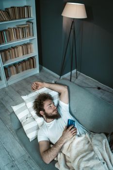 sexy brutal man with curly hair and a beard fell asleep with his Smartphone on the couch. sleep separately, guest room. Top view. Close-up. High quality photo