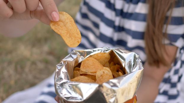 The girl eats chips in the city park in the summer. The girl eats chips in the city park in the summer. Package with chips close-up