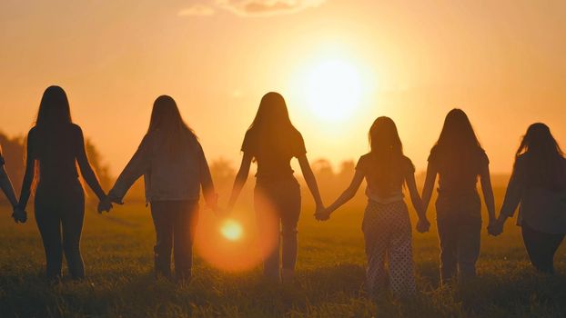 Eleven cheerful girls run to the meeting across the field in the summer, holding hands