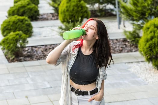 A beautiful woman drinking water from a reusable silicone sport bottle on a sunny day in the city