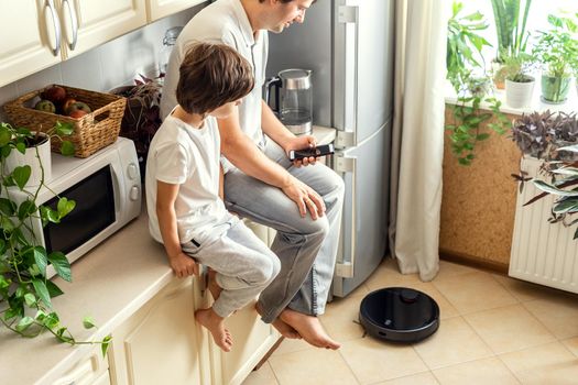 Happy Father and Son Operating Robotic Vacuum Cleaner With Smartphone Remote Control in the Kitchen