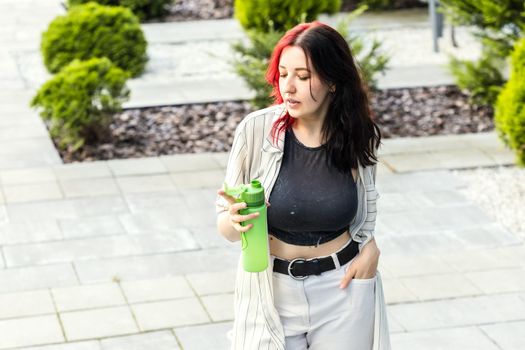 Stylish woman carry her own reusable water bottle, standing outdoors. Stay hydrated, Eco friendly, zero waste and green living lifestyle concept.