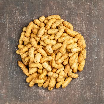 Heap of the peanuts with the shell. Not peeled groundnuts shelled - top view on wooden background