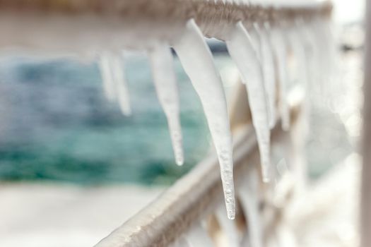 Frozen jetty at the sea with icicles hanging at the metal handrails. Shallow depth of field