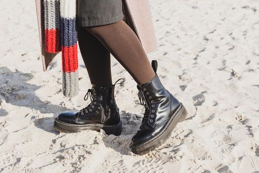 Stylish black smooth leather ankle boots in outdoor on the sand beach. Cold season outfit