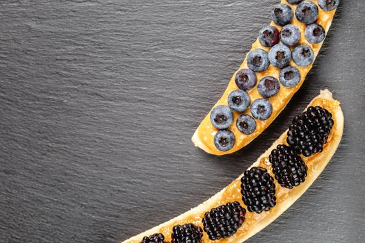 Healthy appetizers with sliced bananas with peanut butter spread, blueberries and blackberries on the top on the slate plate, space for text