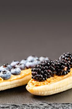 Healthy appetizers with sliced bananas with peanut butter spread, blueberries and blackberries on the top on the slate plate, space for text