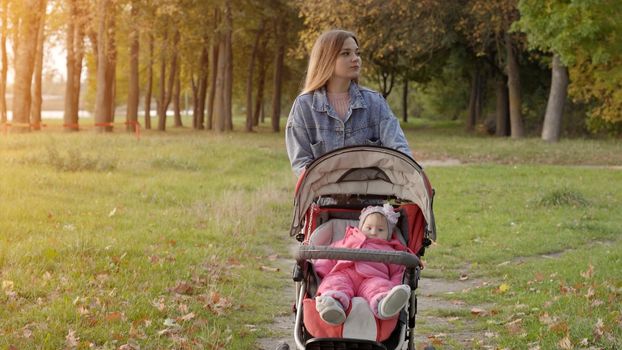 A young mother with a stroller walks in the autumn evening