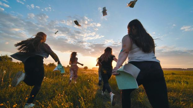 Cheerful students run throwing notebooks after school at sunset