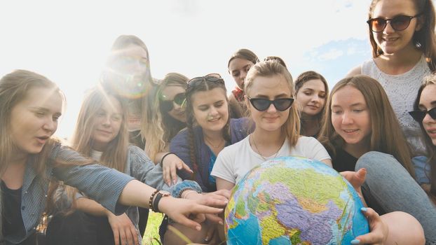 A group of cheerful girls is exploring the globe of the world in the meadow