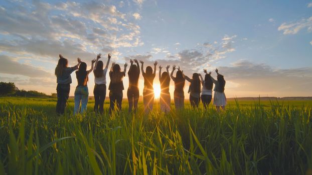 Silhouette of friends of 11 girls waving their hands at sunset in the field