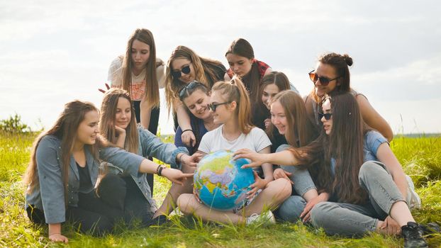 A group of cheerful girls is exploring the globe of the world in the meadow