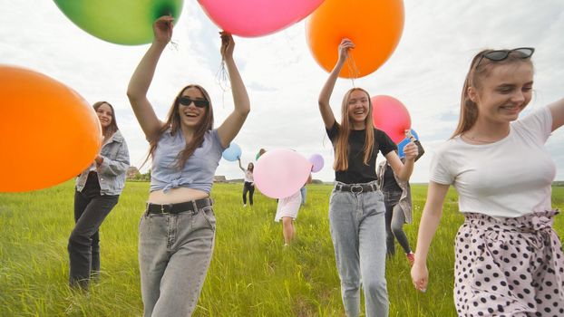 Girls friends are walking across the field with large balloons and colorful balloons