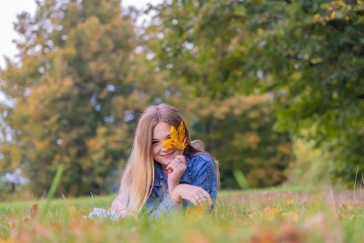 A young girl lies on the grass in a warm autumn in the evening with a petal in her hands