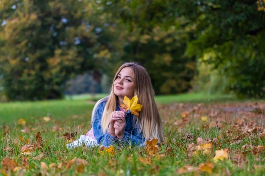 A young girl lies on the grass in a warm autumn in the evening with a petal in her hands