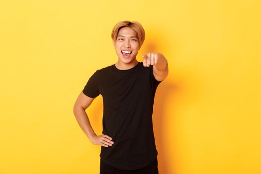 Portrait of cheerful handsome asian guy with blond hair choosing you, smiling and pointing finger at camera, congrats gesture.