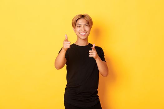 Portrait of cheeky smiling asian guy, looking satisfied and pointing fingers at camera, praising something or making compliment.