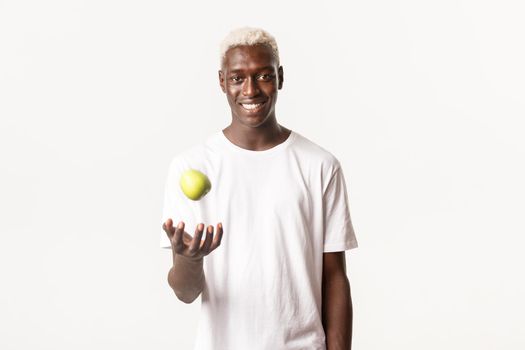 Portrait of sassy handsome african-american blond guy, catching apple and smiling confident, standing white background.