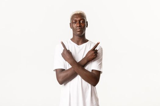 Portrait of confident blond african-american man, pointing fingers sideways, showing variants of choices, standing white background.