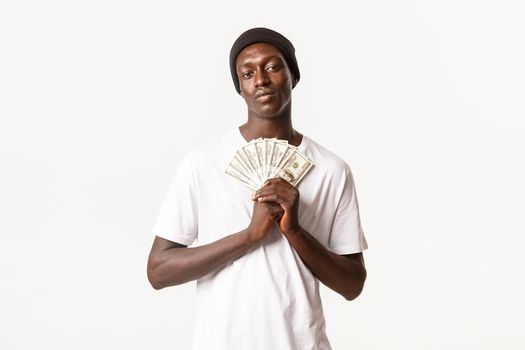 Portrait of pleased confident african-american guy, looking at camera determined while holding money, white background.